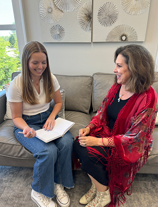 A woman sitting on top of a couch next to another person.